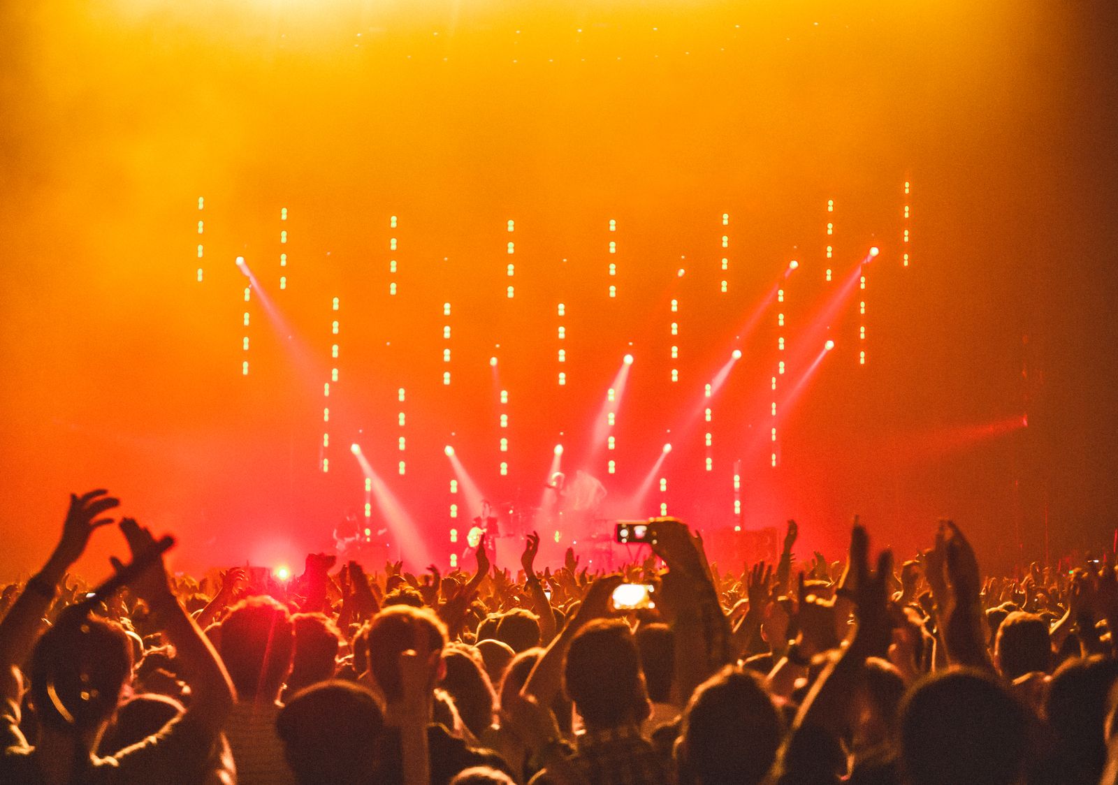 Energetic concert crowd with hands raised in front of bright stage lights, representing the live-event audience experience
