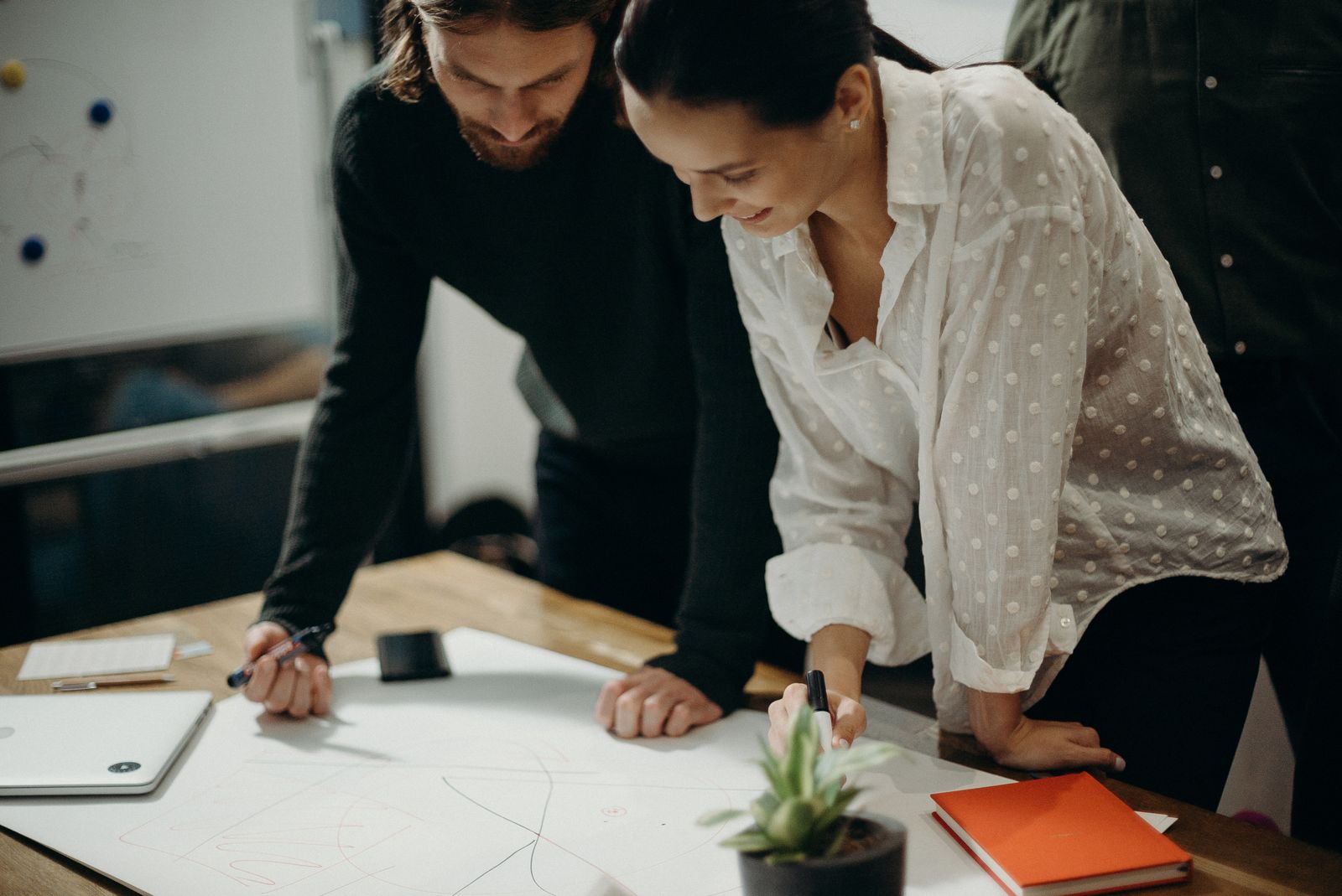 Two colleagues at a whiteboard in a brainstorming session, illustrating UX strategy work
