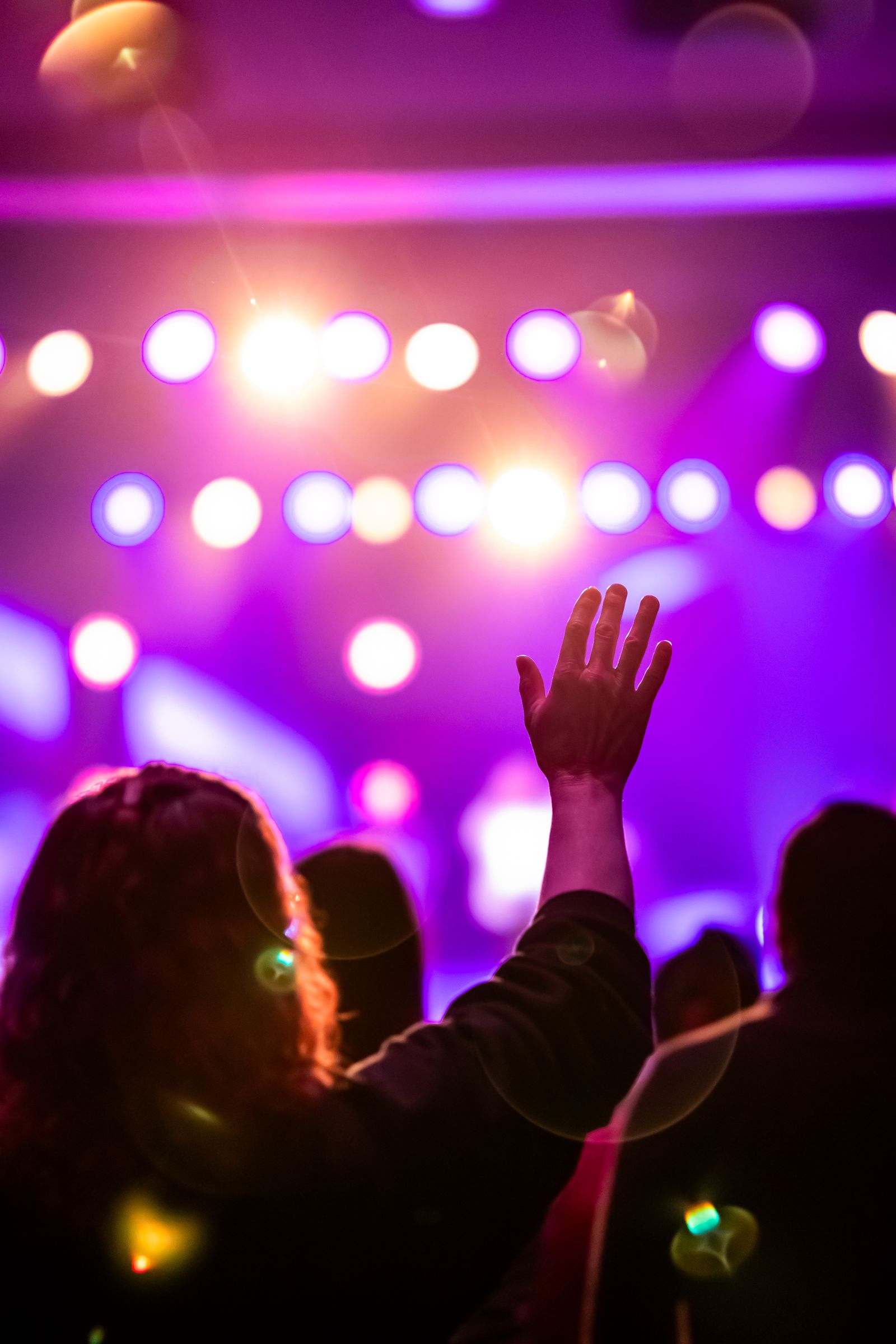 Single audience member's hand raised in a spotlight amid a vibrant concert, symbolising the individual experience a UX architect advocates for