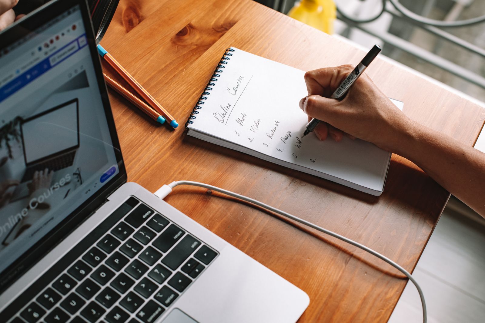 Person writing research notes beside a laptop, representing UX research and discovery tools