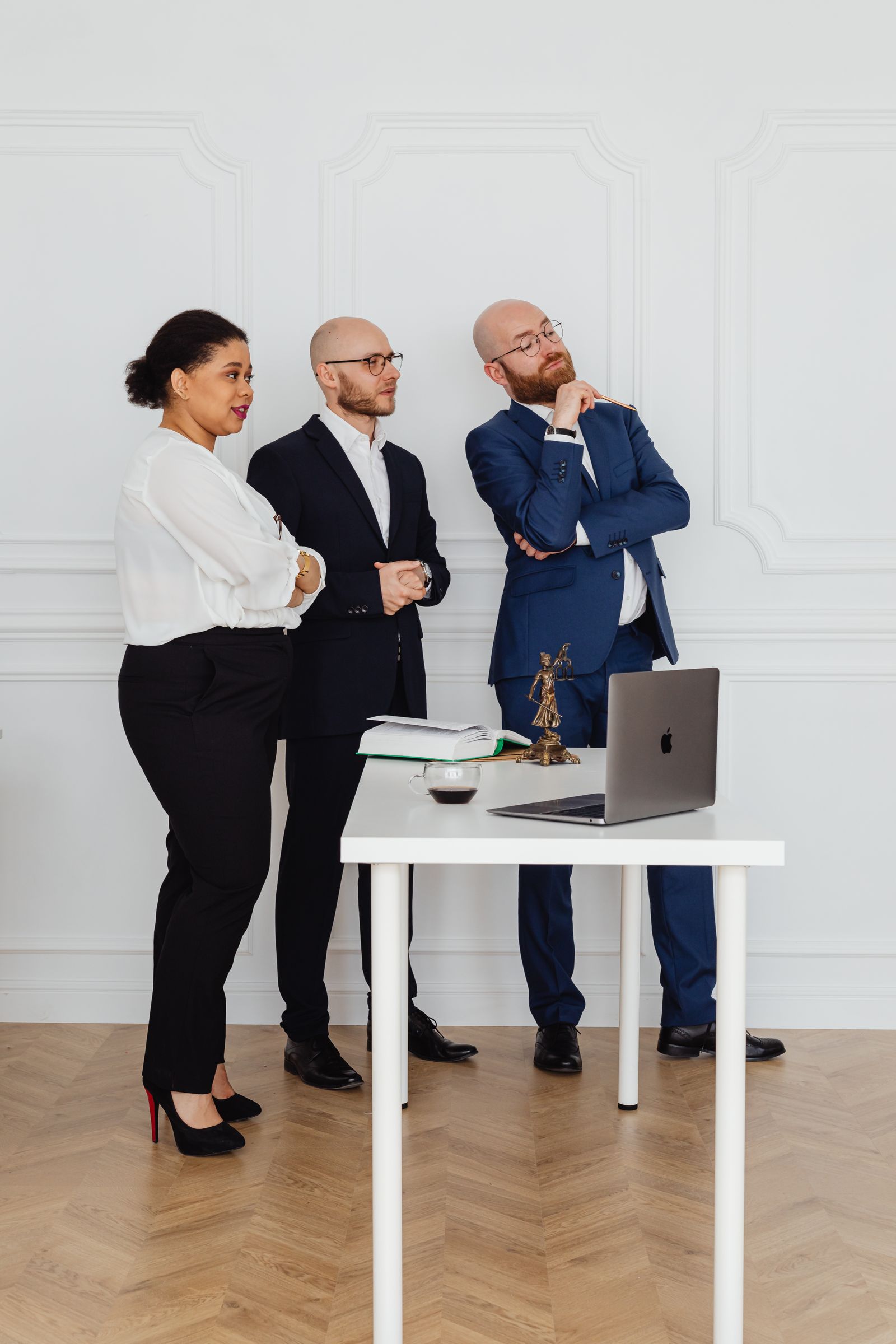 Business professionals standing around a desk with a laptop, discussing a plan