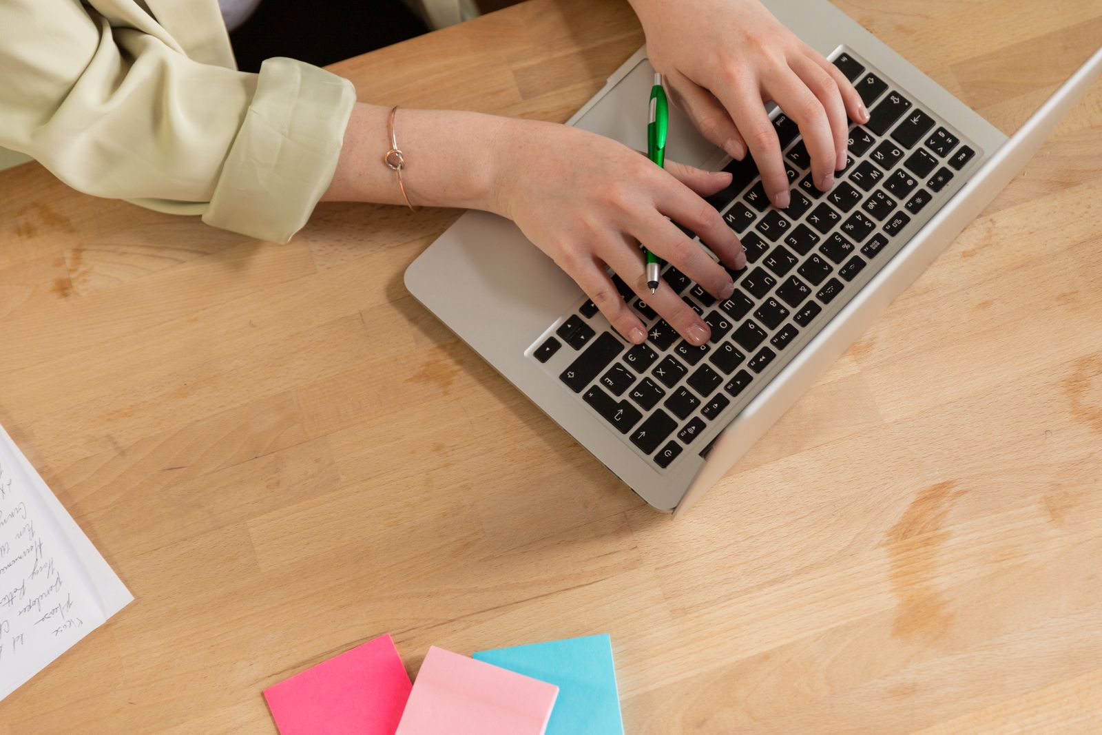 Hands typing on a laptop with a pen and sticky notes, showing a UX designer's daily workflow